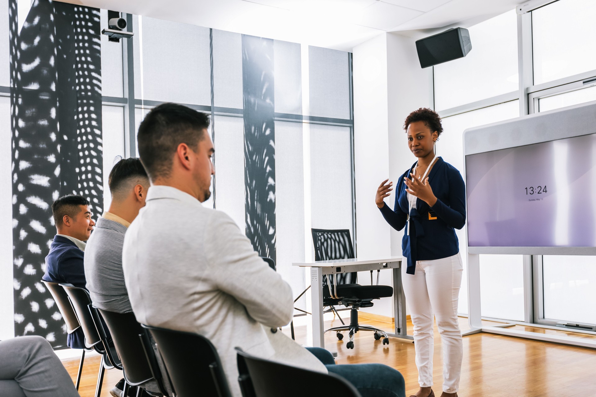 African American woman CEO standing in front of a multiracial group of colleagues. Multimedia classroom with smart board and graphics on them.